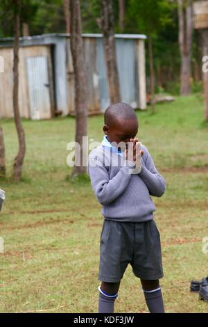 Young african school boy in uniform bows his head in prayer in the school yard Stock Photo