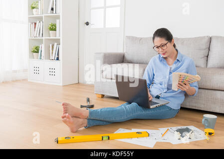 smiling attractive designer lady using mobile computer searching new house plan information and holding palette tool choosing design color. Stock Photo