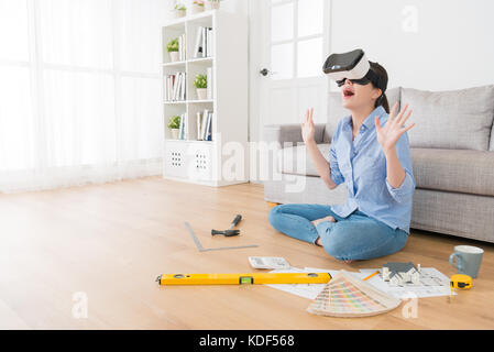 cheerful young woman feeling surprised when she wearing virtual reality glasses device viewing 3D simulation house construction video. Stock Photo