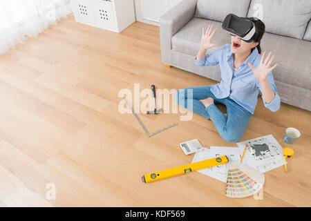 elegant pretty woman wearing VR technology glogges sitting on floor and viewing new house design drawing video feeling surprised. high angle view phot Stock Photo
