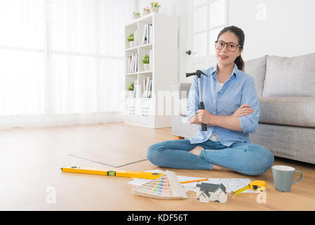 confidence successful female interior engineer holding hammer tool sitting on wooden floor design new working house case and face to camera smiling. Stock Photo