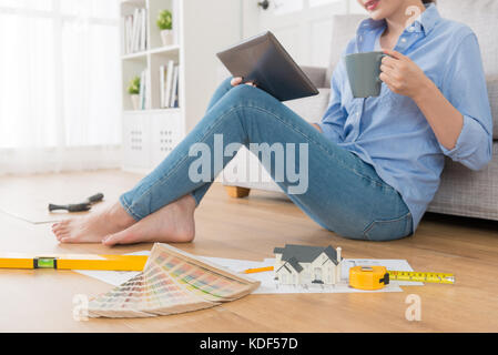 closeup photo of beautiful woman drinking hot coffee using mobile pad computer and doing house interior design work with engineer tool in living room  Stock Photo