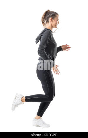 Happy smiling female jogger running in zip up hooded sweatshirt and leggings. Side view. Full body length portrait isolated on white background. Stock Photo