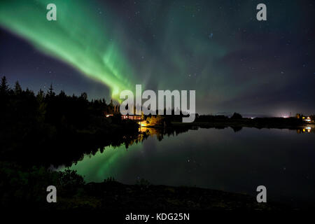 A beuatiful lakehouse in Iceland under the northern lights which reflect in the calm waters of the lake, very peaceful and calm Stock Photo