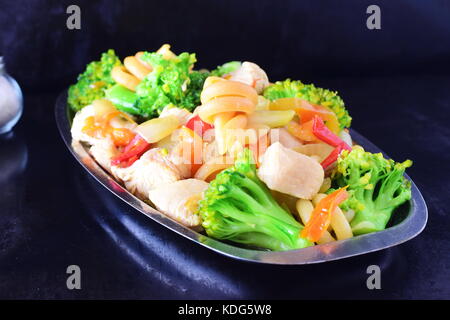 Stir fried chicken fillet with vegetables and pasta on a metal tray on a black abstract background. Stock Photo