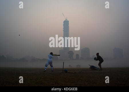 Cricket is being played on a winter morning with a high rise building in the background.