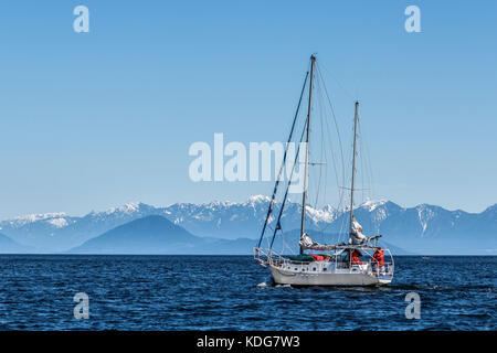 A sailboat sets out across BC's Strait of Georgia on a cold, clear day in early spring (Bowen Island, Howe Sound and Coast Range in background). Stock Photo