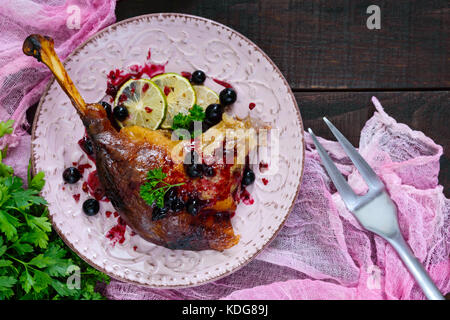 Fried goose leg in berry sauce on a ceramic plate on a dark wooden background. Top view. Stock Photo