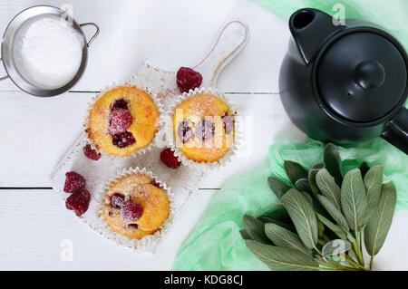 Delicious freshly baked muffins with raspberries, decorated with powdered sugar, teapot on a white wooden background. Top view. Stock Photo