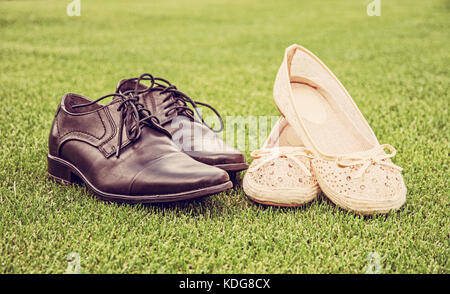 Women's and men's wedding shoes on the green grass. Symbol of love. Retro photo filter. Stock Photo