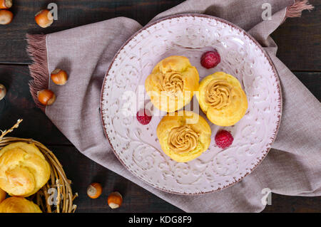 Delicious profiteroles with caramel nut cream on a ceramic plate on a dark wooden background. Top view. Stock Photo