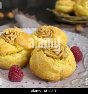 Delicious profiteroles with caramel nut cream on a ceramic plate on a dark wooden background. Stock Photo