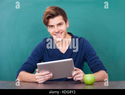 Man Using Holding Digital Tablet In Front Of Green Chalkboard Stock Photo