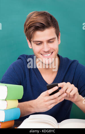 Happy Male Student Using Cellphone While Studying Stock Photo