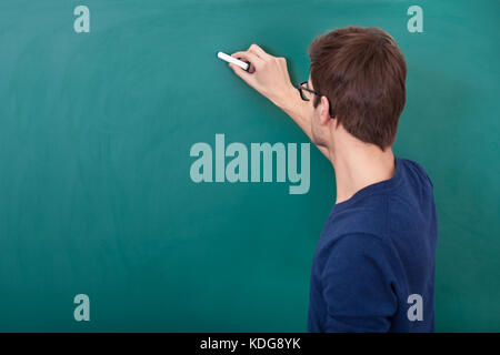 Rear View Of A Male Student Writing On Chalkboard With Chalk Stock Photo