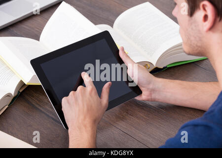 Male Student Surrounded By Books Using Digital Tablet Stock Photo
