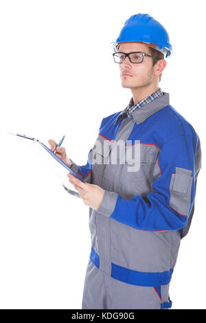 Young Construction Reviewer Wearing Workwear And Hardhat Writing On Clipboard Stock Photo