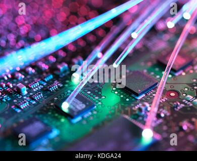 Fibre optic strands carrying data, with electronics in the background. Stock Photo