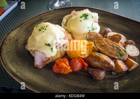 Delicious Benedict Eggs served with baked patatoes and tomatoes on dark plate Stock Photo