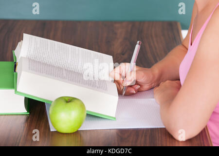 Portrait of young female student writing on paper beside green apple Stock Photo