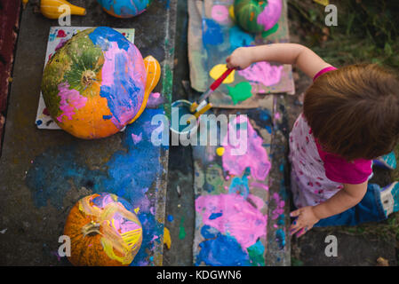 A little girl paints pumpkins during autumn activities. Stock Photo