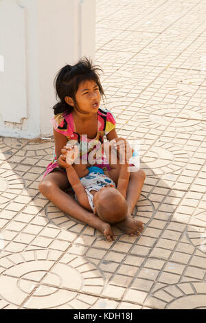 PHNOM PENH, CAMBODIA - FEBRUARY 21, 2013: An unidentified child with an unidentified baby sit begging for money on the street in Phnom Penh Stock Photo