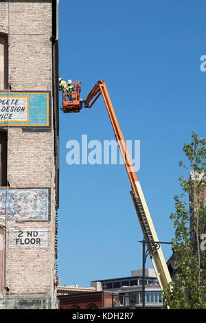 Grand Rapids, Michigan - Two men on a cherry picker work on the side of an old downtown building. Stock Photo