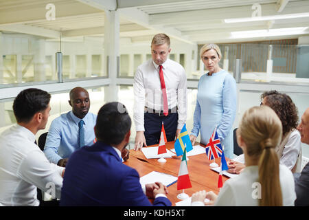 Young and mature politicians standing by table and listening to their foreign colleagues during discussion of strategies Stock Photo