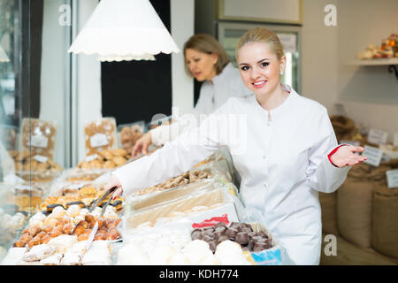 Smiling blonde woman offering fresh and tasty pastry in bakery Stock Photo