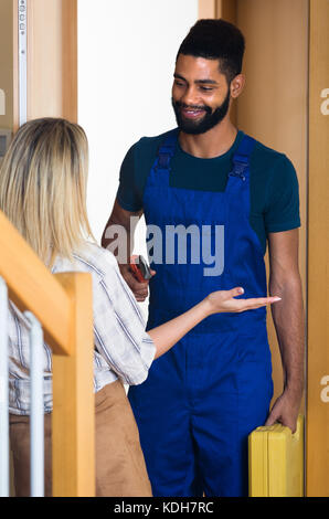 Girl meeting smiling African handyman in blue overall at the doorway Stock Photo