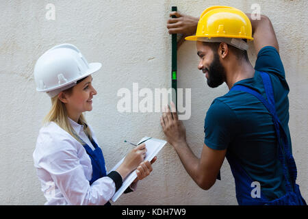 Smiling female engineer and black specialist checking wall plane Stock Photo