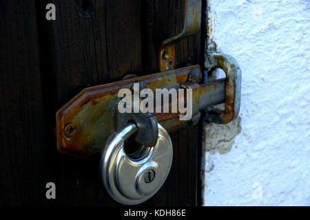 metal padlock on rusty door hinge with peeled paint Stock Photo