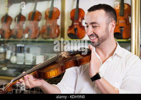 Cheerful man with beard purchasing traditional violins in store Stock Photo