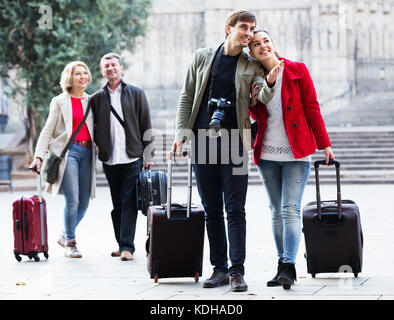 Two couples of tourists in casual with luggage stroll along the streets outdoors Stock Photo