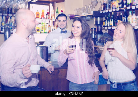 Happy man drinking coffee and talking to two beautiful women with glasses of wine in a bar Stock Photo