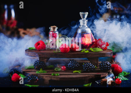 Raspberry and blackberry perfume in a vintage bottle. Dark still life with wintage wooden shelves and fresh berries. Aromatic laboratory concept, magi Stock Photo