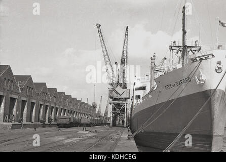 1960s, historical, the container ship, City of Oxford, moored at London Docks, London, England, UK. In the picture are the rail freight wagons beside storage depots. Built in 1948 in Glasgow on the Clyde by John Brown & Co for Ellerman Lines, the cargo ship was steam-powered and survived until 1978 when it was broken up. Stock Photo