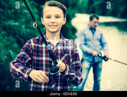 Happy teenage boy fishing on freshwater lake from shore Stock Photo