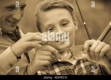 portrait of cheerful teenager boy holding catch fish on hook at fishing with father Stock Photo