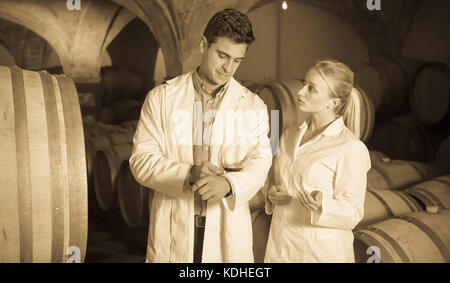 Two speaking wine house workers checking quality of product in cellar Stock Photo