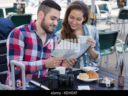 Young european couple drinking coffee in street restaurant and learning map Stock Photo