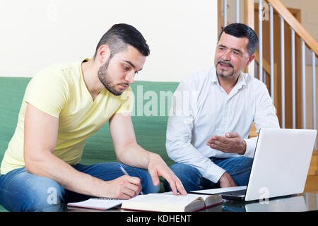 Smiling mature father helping adult son to do homework. Focus on the left man Stock Photo