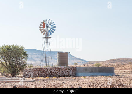 A farm scene with a water-pumping windmill and dam at Bergsig, a small village in the Kunene Region of Namibia Stock Photo