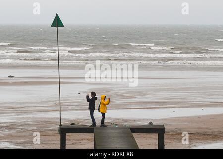 Seascale, Cumbria, England, UK. 14th Oct, 2017. UK weather - a couple taking photographs on a blustery day with low cloud at Seascale Beach, Cumbria Credit: Kay Roxby/Alamy Live News Stock Photo