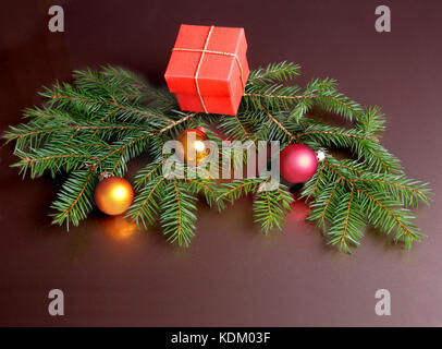 Christmas gift red box, colored balls and christmas tree on dark mirror table. Celebrities composition. Selective focus. Stock Photo