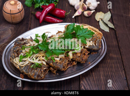 fried fish crucian with onions on an iron plate, top view