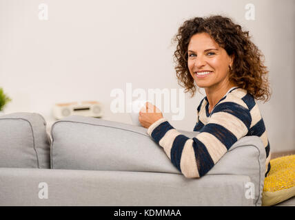 Beautiful woman sitting on the sofa and drinking a coffee Stock Photo