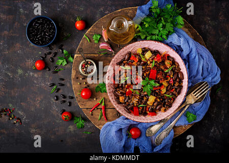 Stewed black beans with sweet peppers and tomatoes with spicy sauce in a pink bowl Stock Photo