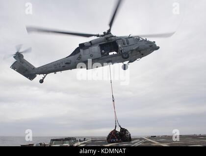 An MH-60S Sea Hawk helicopter delivers supplies to a ship. Stock Photo
