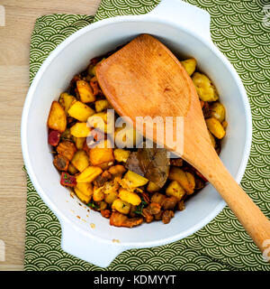 French cuisine Lardons - Fried cubed pork belly , bacon and cubed potato with thyme ,bay leaves and galic  in a white bowl set up on wooden table flat Stock Photo